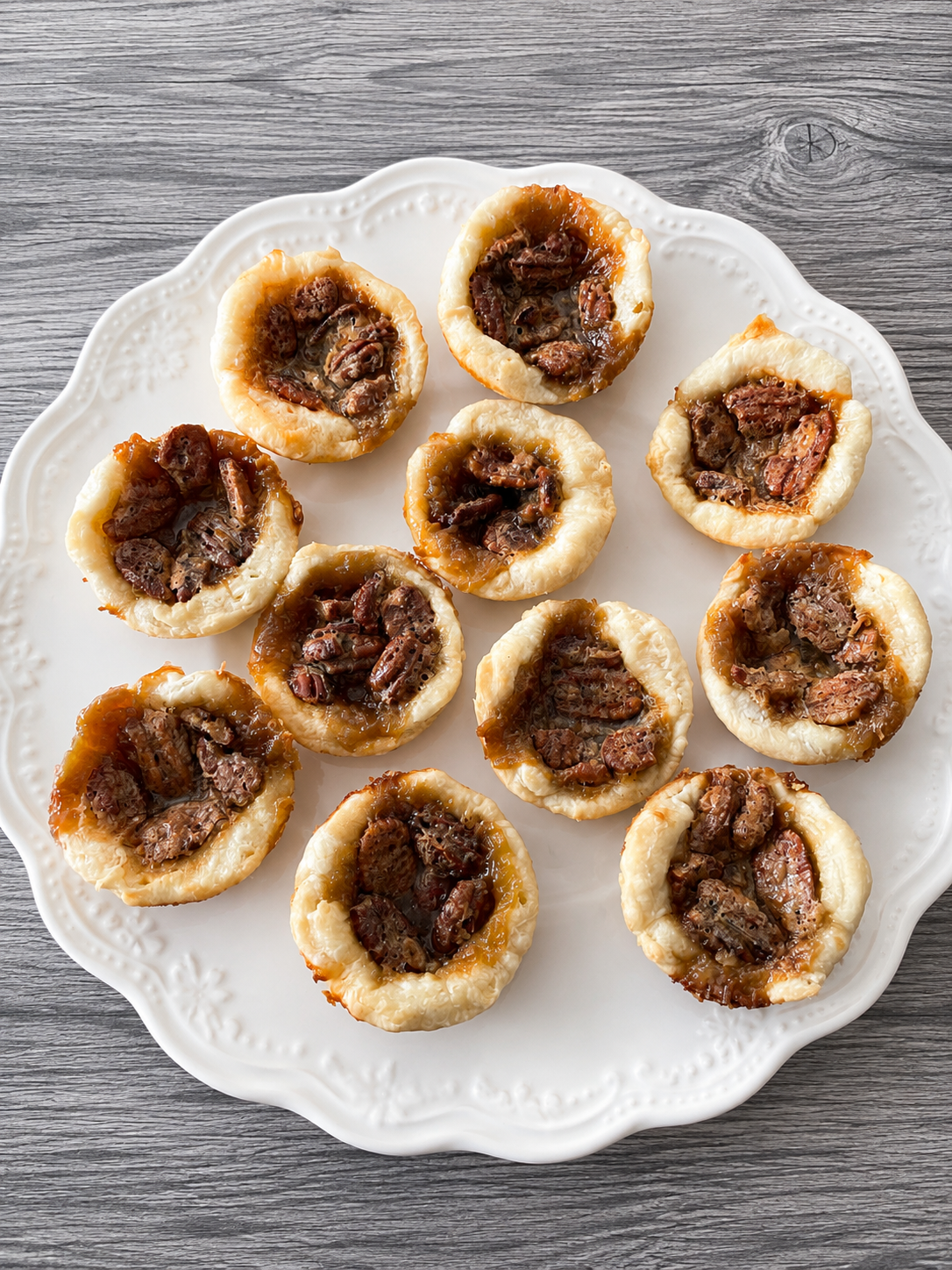 Mini butter tarts with pecan halves, golden pastry tartlets on a white plate