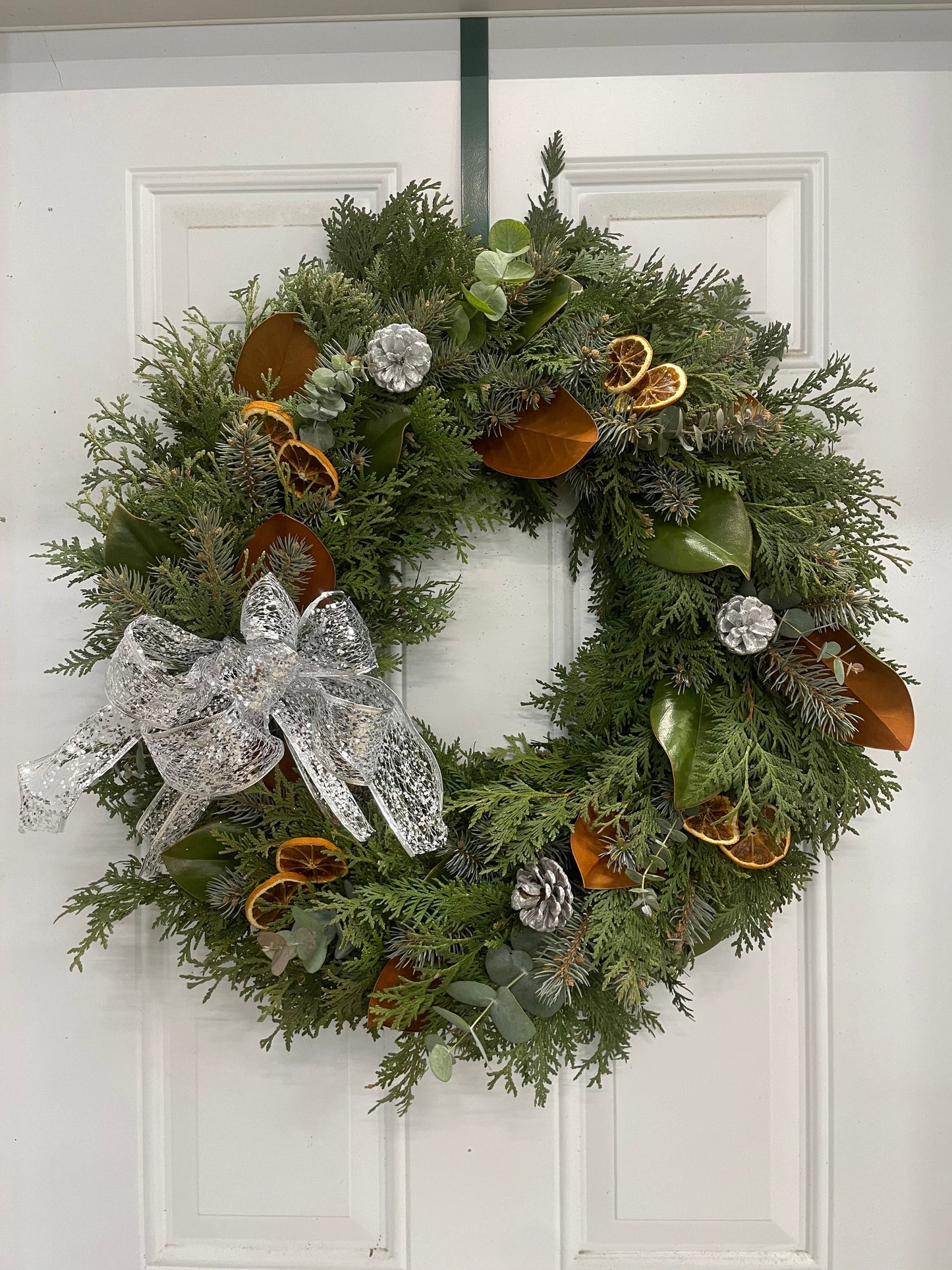 Handcrafted Christmas wreath with green branches, large silver bow, pinecones and silver ornaments