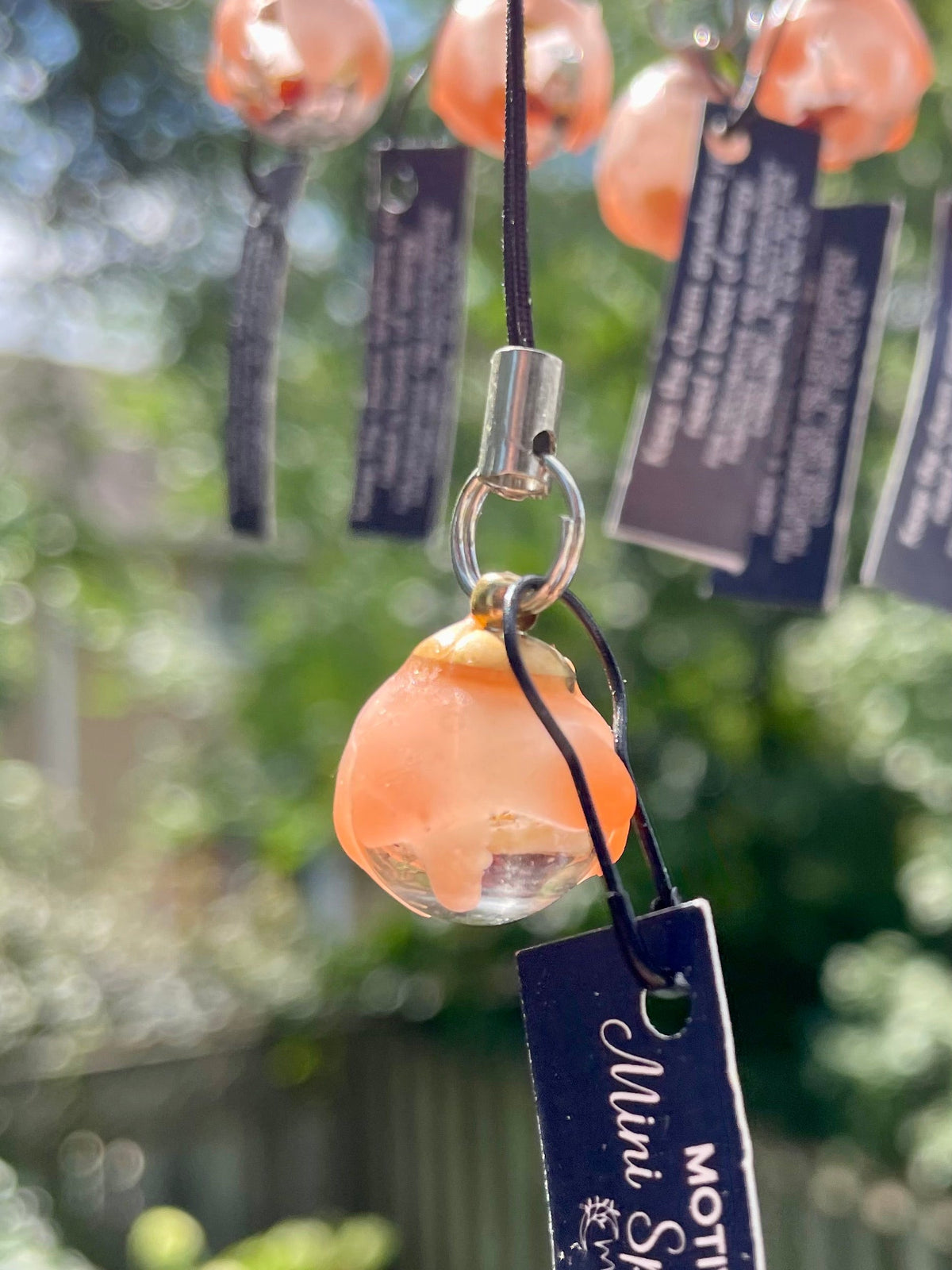Orange translucent charm with silver loop and navy motivation tag on black cord