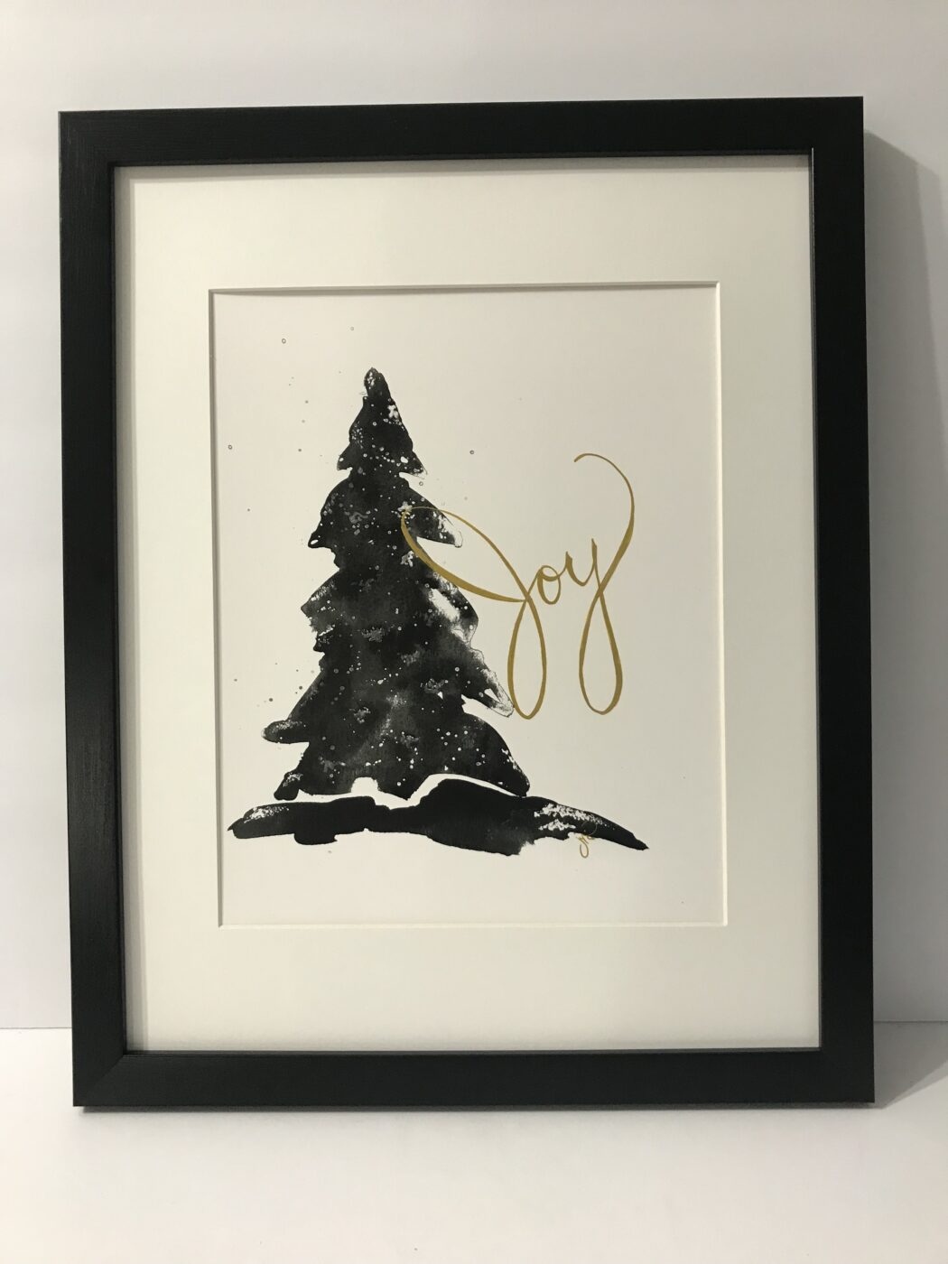 Framed wall art with black Christmas tree silhouette and gold 'Joy' script.