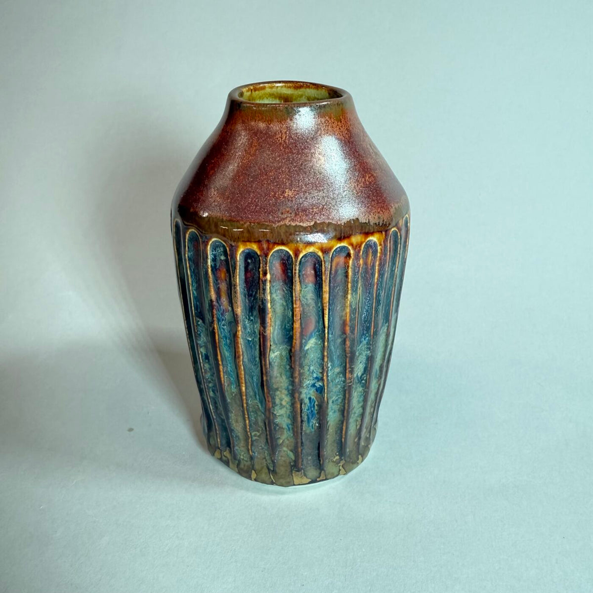 Bud vase in rich copper-brown with blue-green drip glaze and rounded narrow body