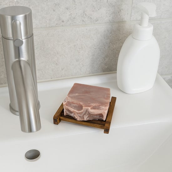 Wooden soap dish with rectangular slotted base holding a bar of soap on a sink
