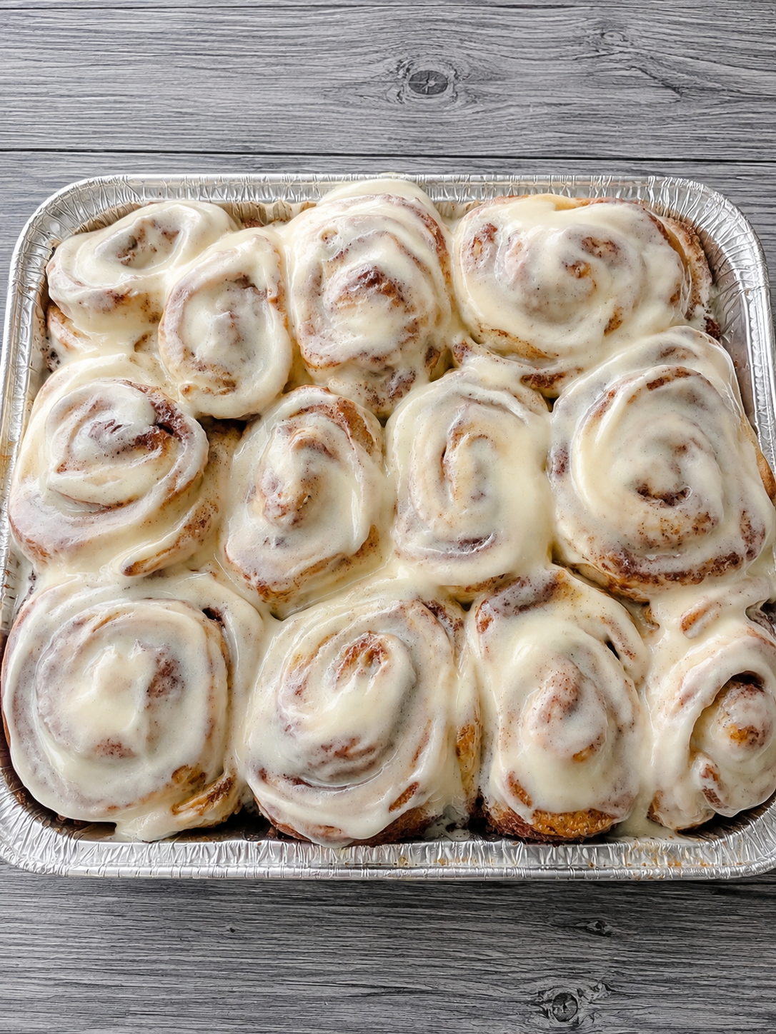 Cinnamon buns in foil tray, swirled tops with cinnamon-brown spots