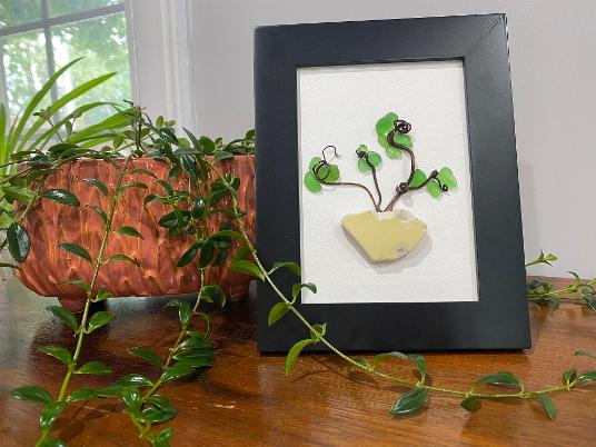 Framed jade-colored leaf and branch wall art with small yellow pendant detail
