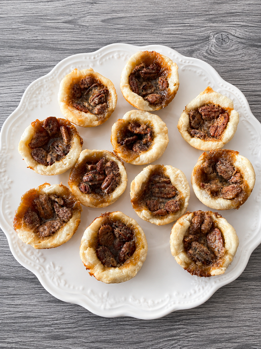 Mini butter tarts with pecan halves, golden pastry tartlets on a white plate