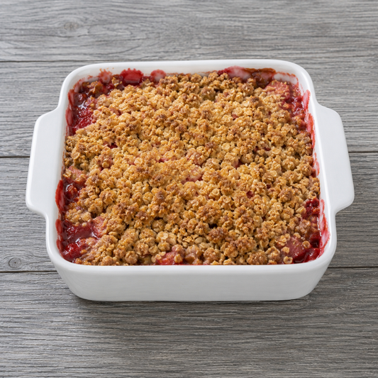 Strawberry rhubarb crisp in white baking dish with golden crumb topping and red fruit filling.