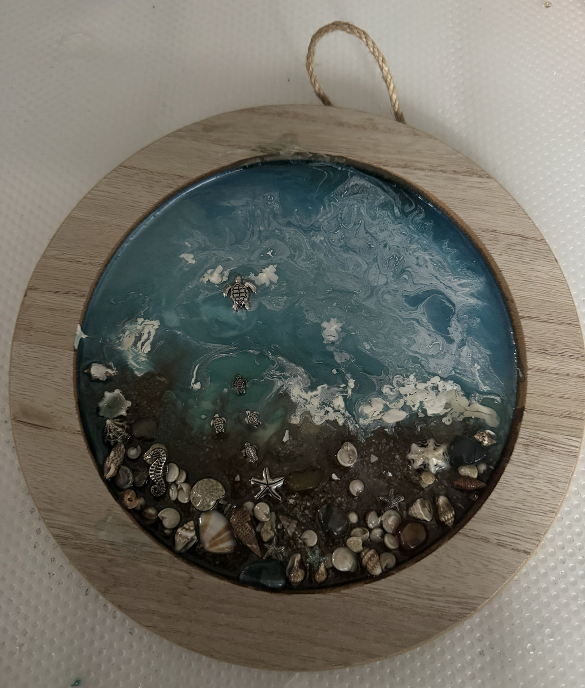 Hanging round acrylic ocean wall frame, teal-blue waves with white foam, shells and starfish