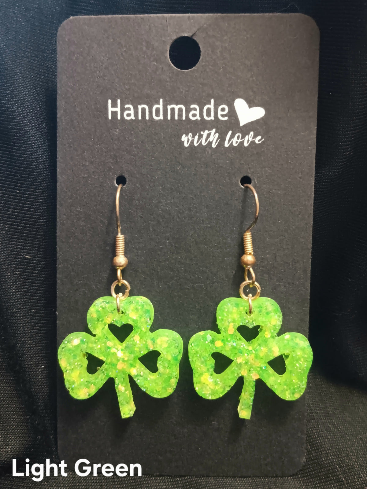 Light green clover dangle earrings with heart cutouts and gold-tone hooks.