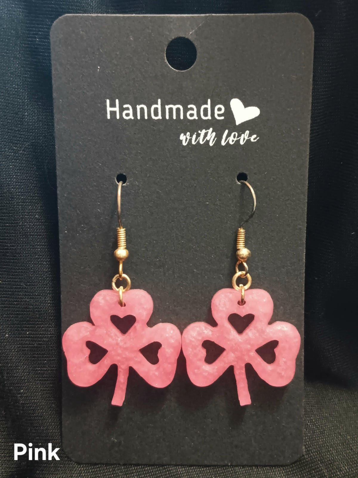 Pink clover dangle earrings with heart cutouts and gold-tone hooks.