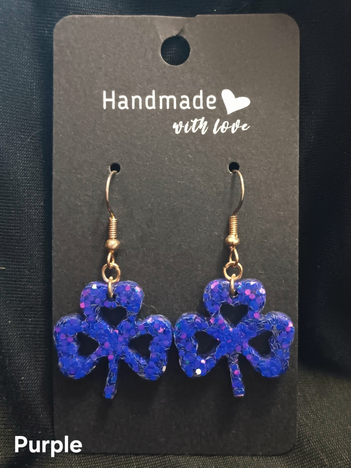 Purple clover dangle earrings with heart cutouts and gold-tone hooks.
