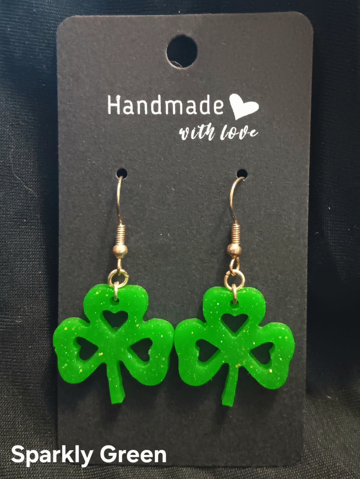 Sparkly green clover dangle earrings with heart-shaped cutouts and gold-tone hooks.