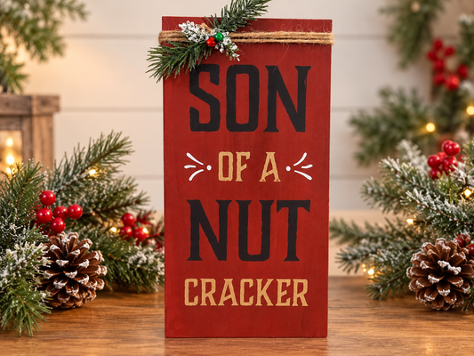 Red rectangular shelf sitter sign with ribbon and "SON OF A NUT CRACKER" text