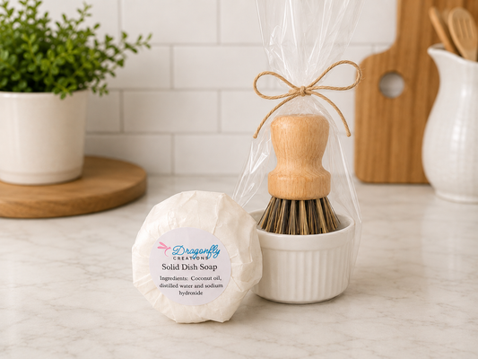 Solid dish soap bar in round white wrap beside a wooden scrub brush