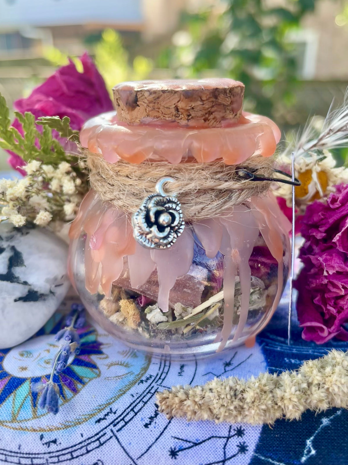 Pink-tinted glass spell jar with cork stopper, dried flowers, and silver charm