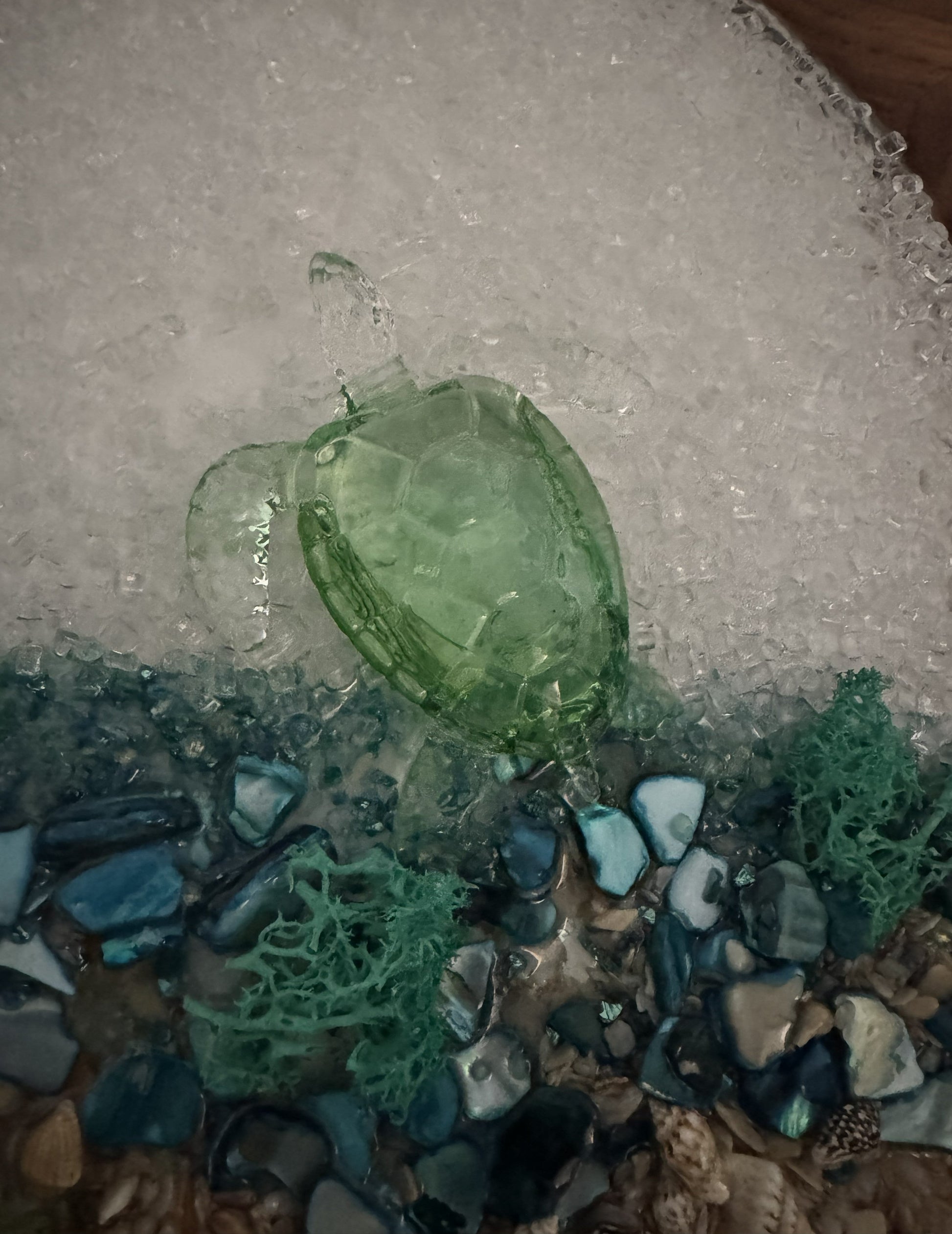 Close-up green glass turtle in sea glass mosaic with blue shards and clear stones