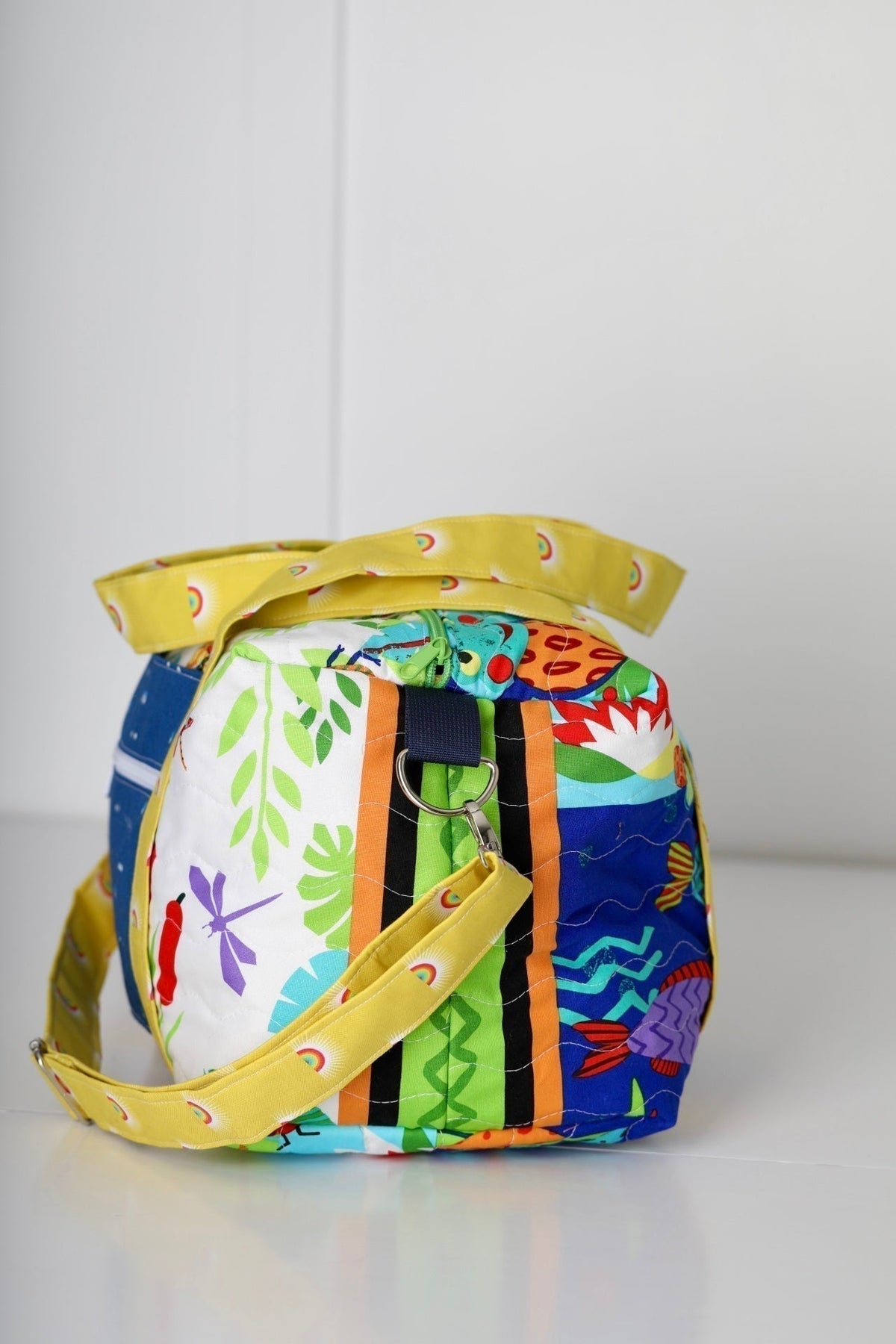 Kids duffle bag with multicolor animal print and yellow webbing straps, side view