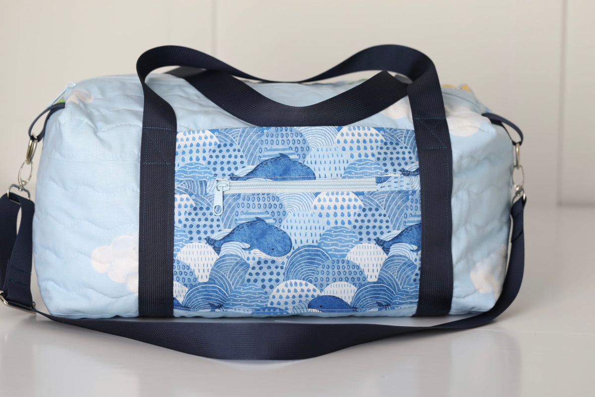 Kids duffle bag with blue whale and wave print and navy side handles, top zipper
