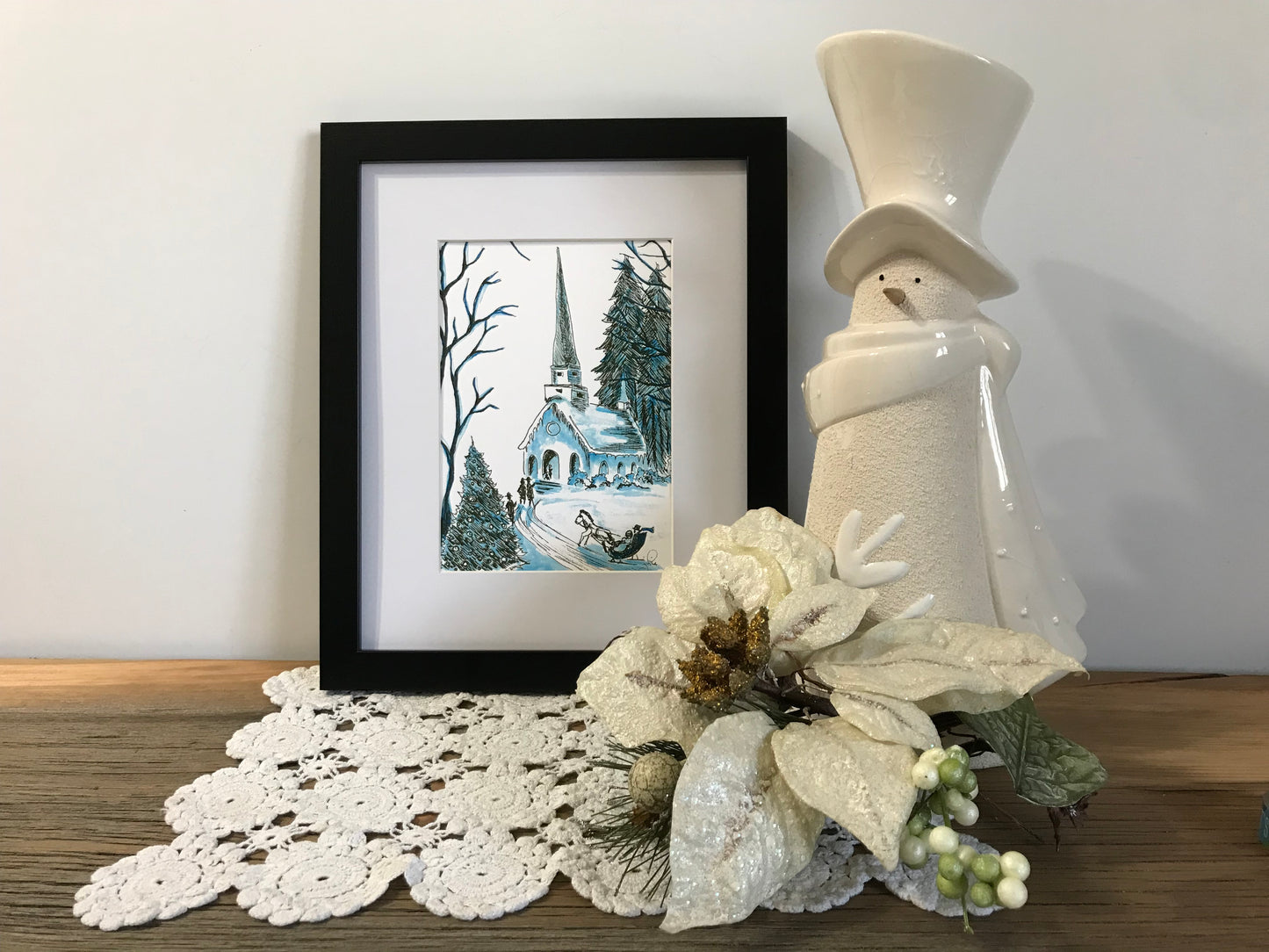 Framed church scene print with winter trees, beside white vase and floral decor