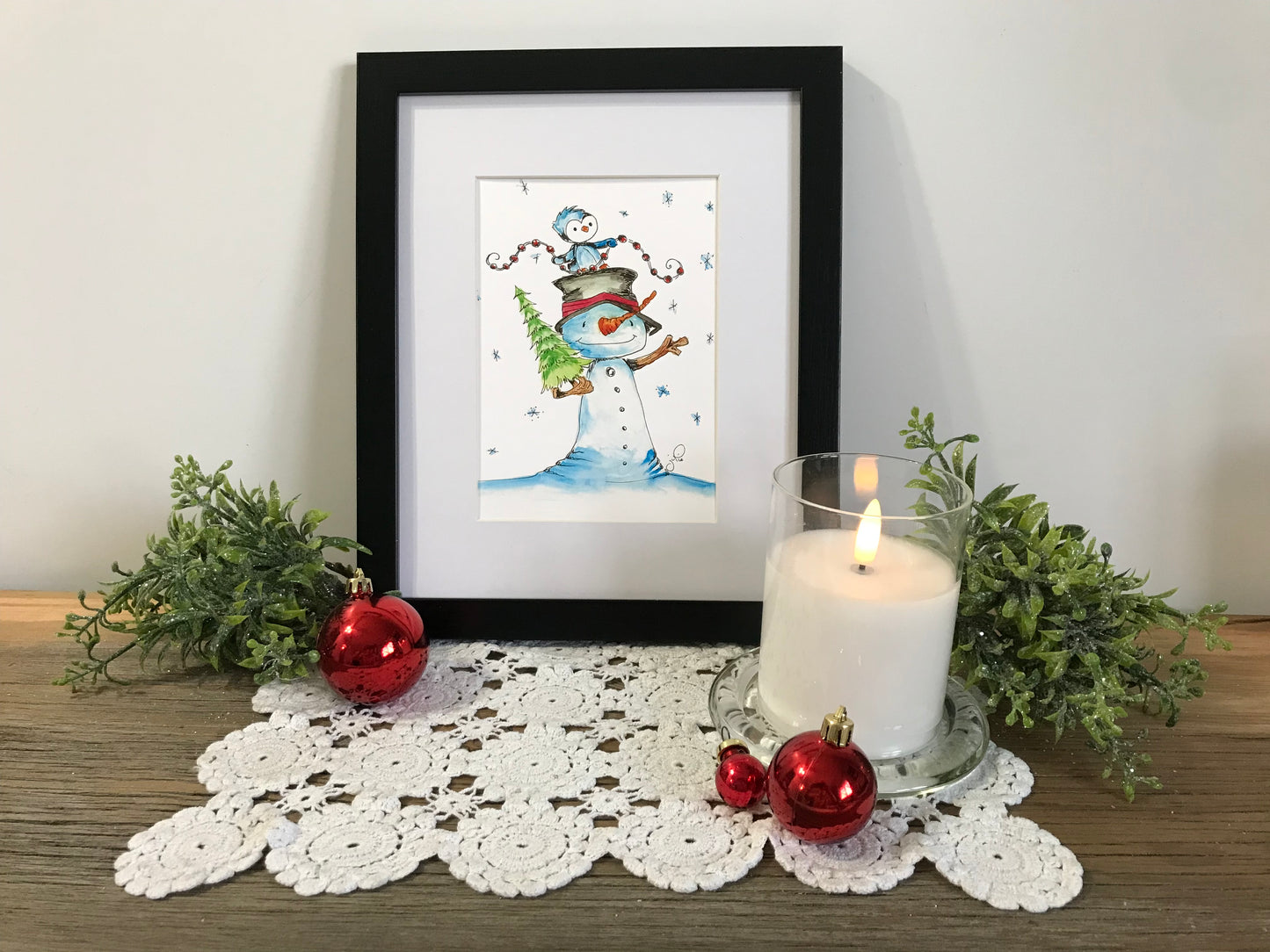 Framed winter illustration with a snowman and penguin characters in a snowy scene