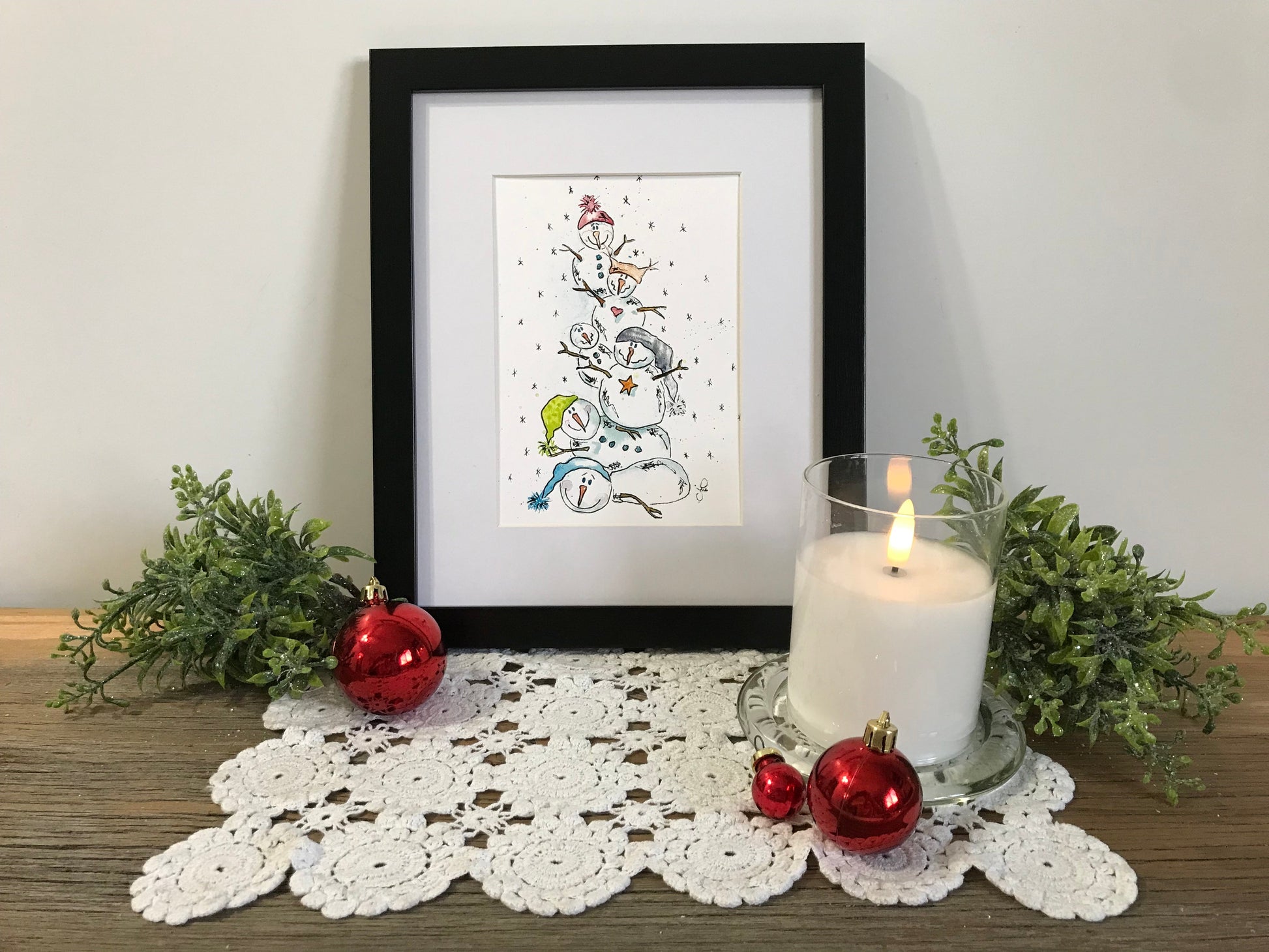 Framed stacked snowmen illustration with small ornaments and winter-themed accents