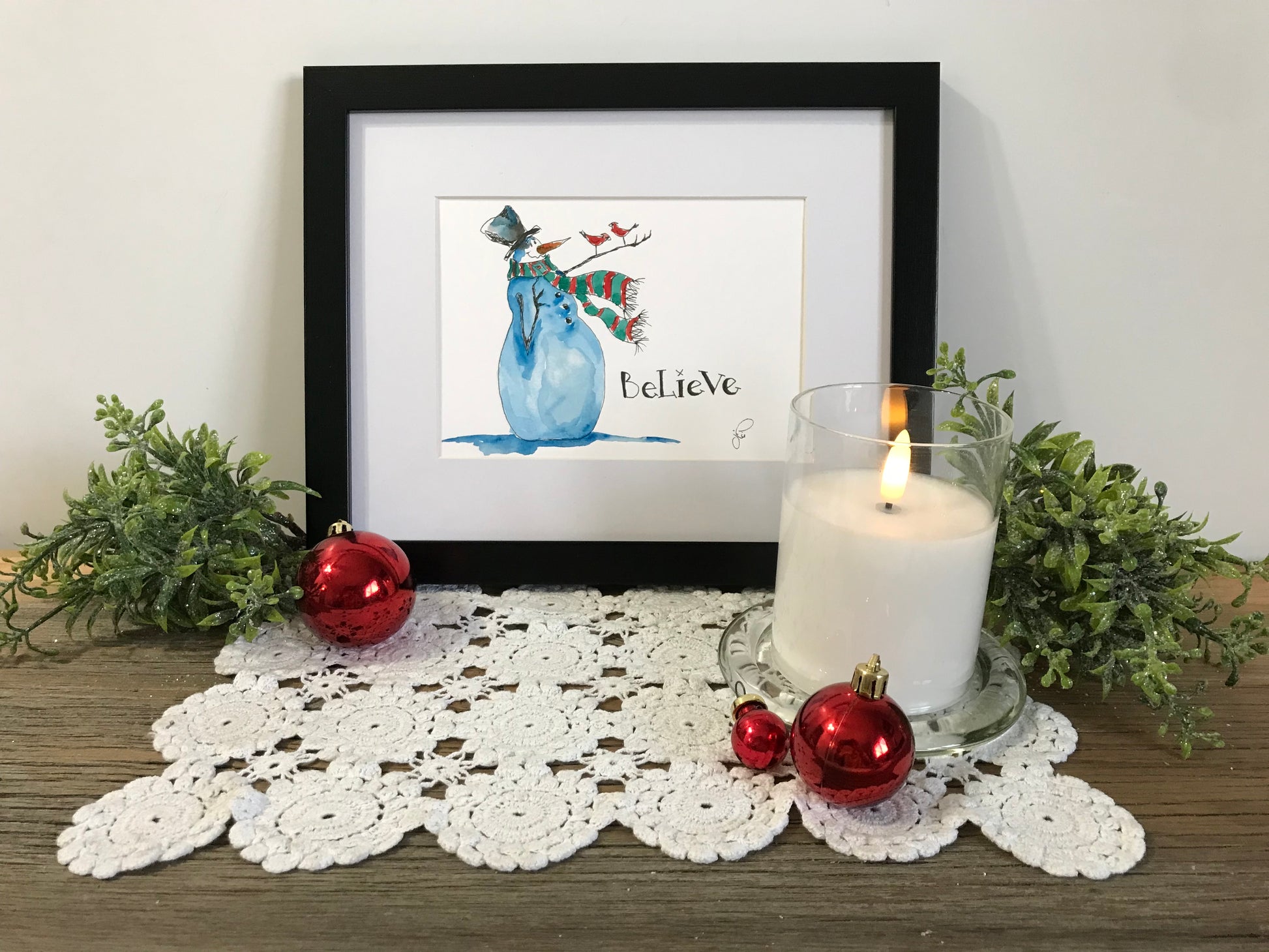 Framed wall art of a blue snowman with teal hat and the word Believe
