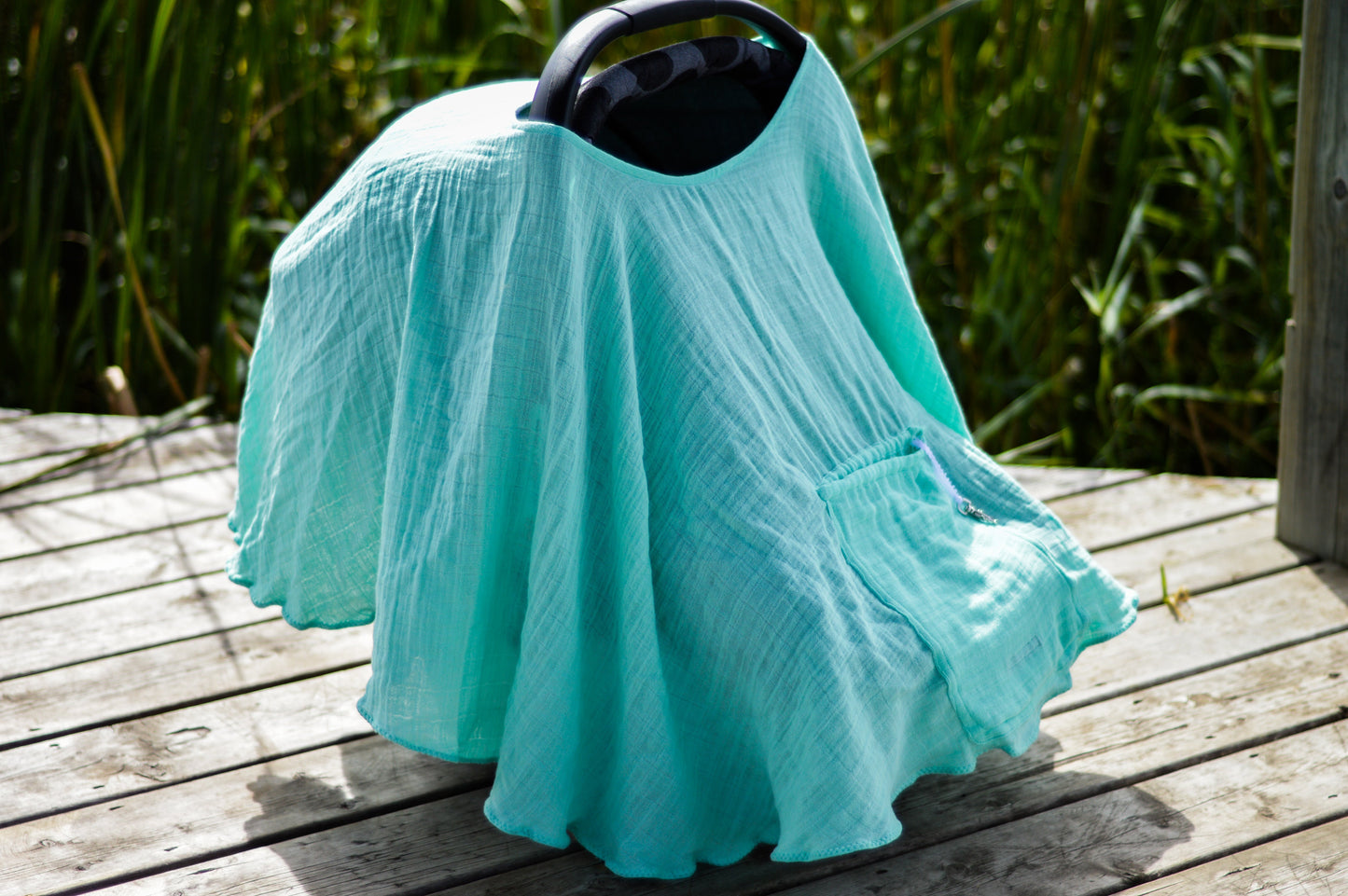 Turquoise nursing cover with black handle, folded on wooden steps