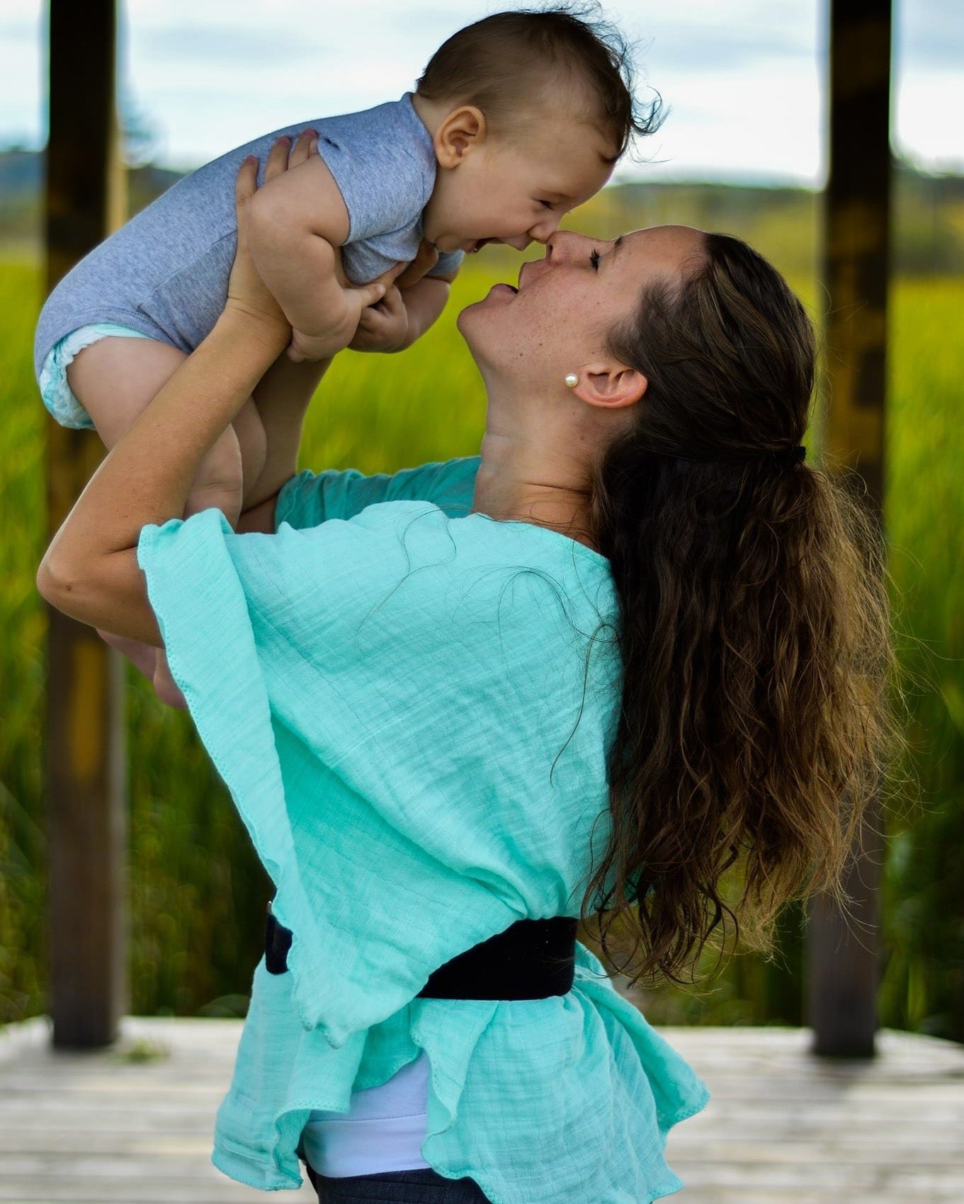 Teal breastfeeding cover draped over parent and baby with black strap