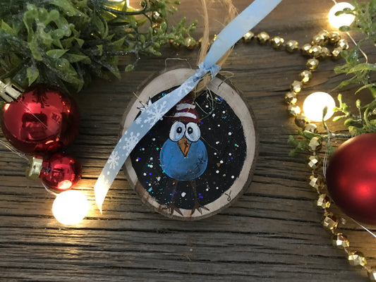 Round painted wooden ornament with blue bird illustration and ribbon hanger