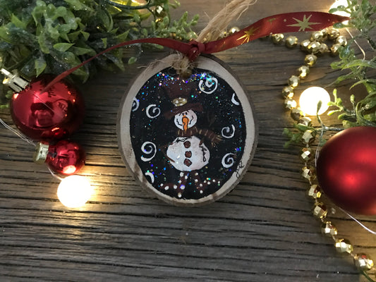 Round hand-painted wooden snowman ornament with blue glitter background and white snowman.