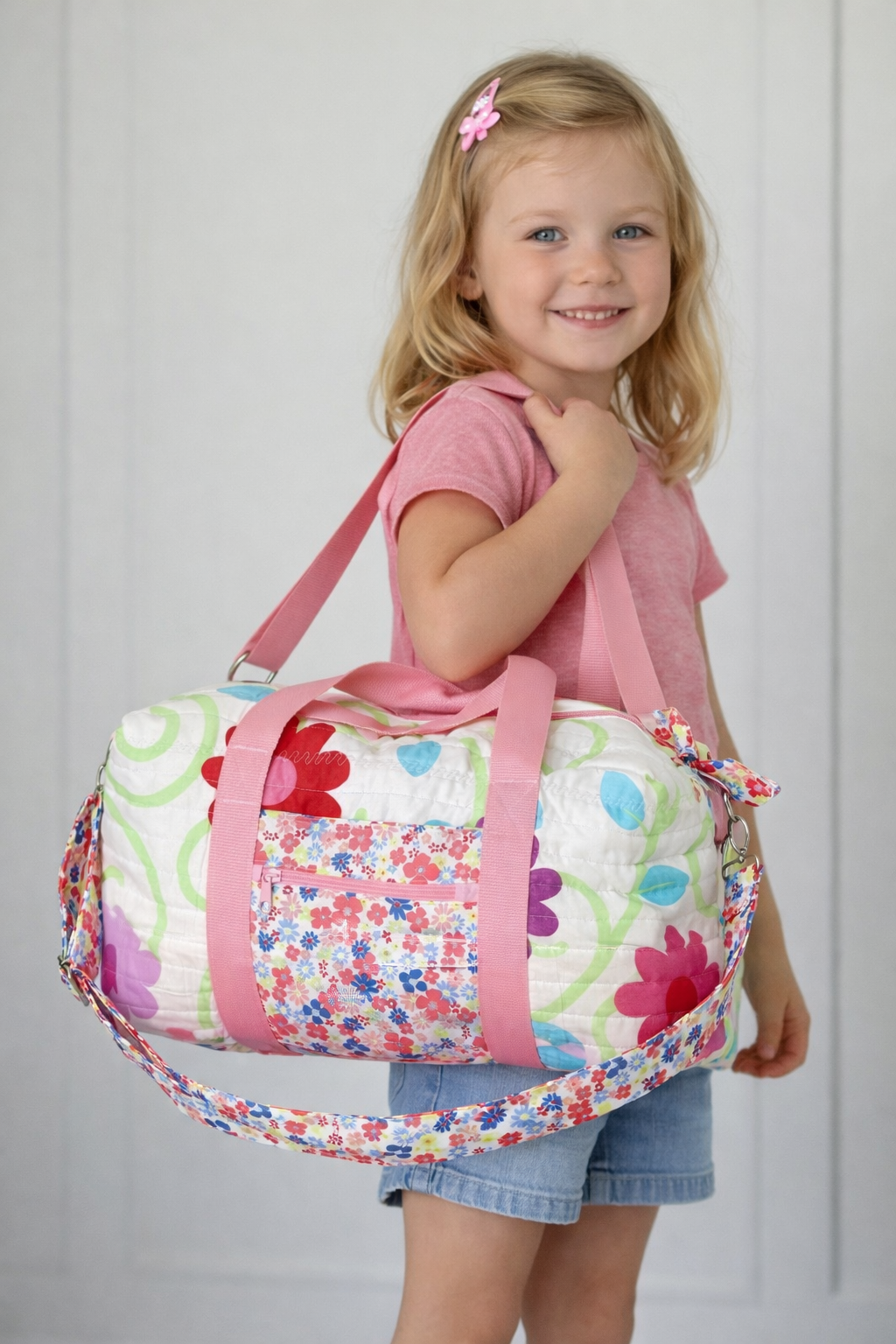 Kids duffle bag with multicolor patchwork print and pink strap accents, held by child