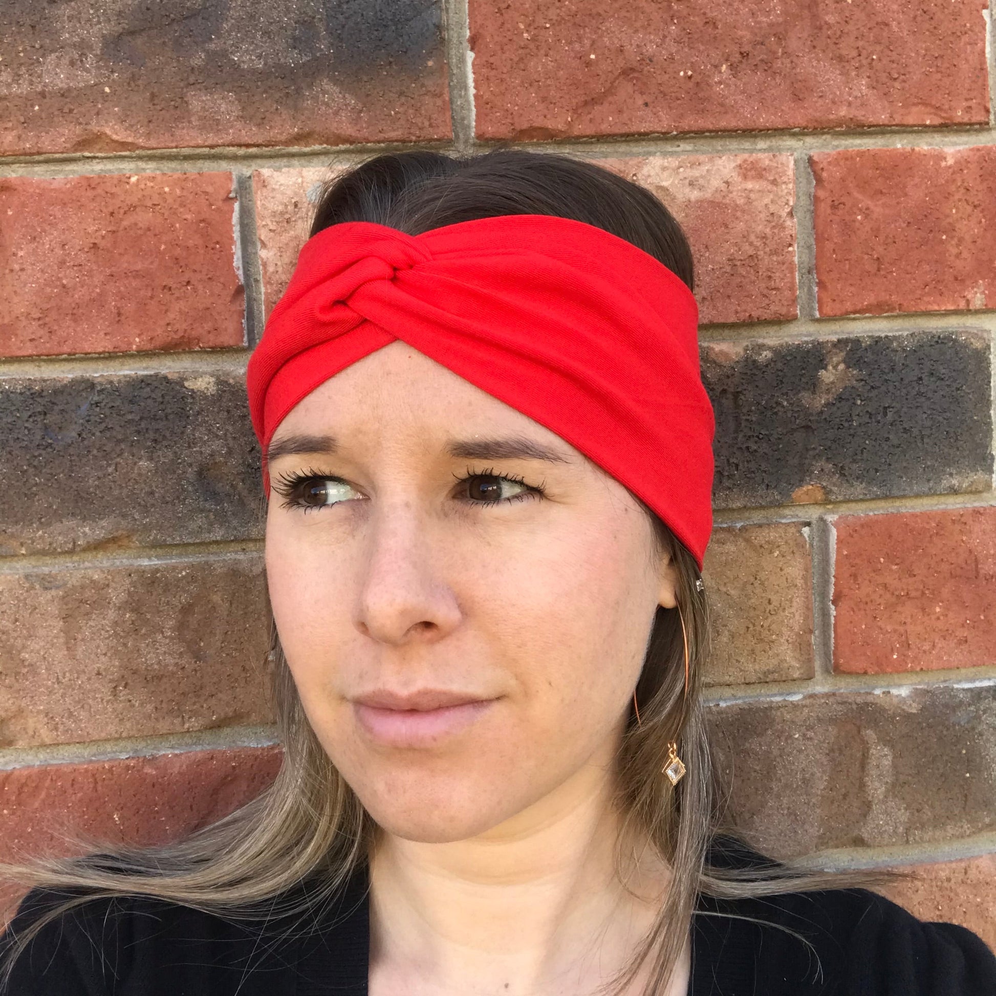 Bright red twist headband with knotted center, close-up on forehead.
