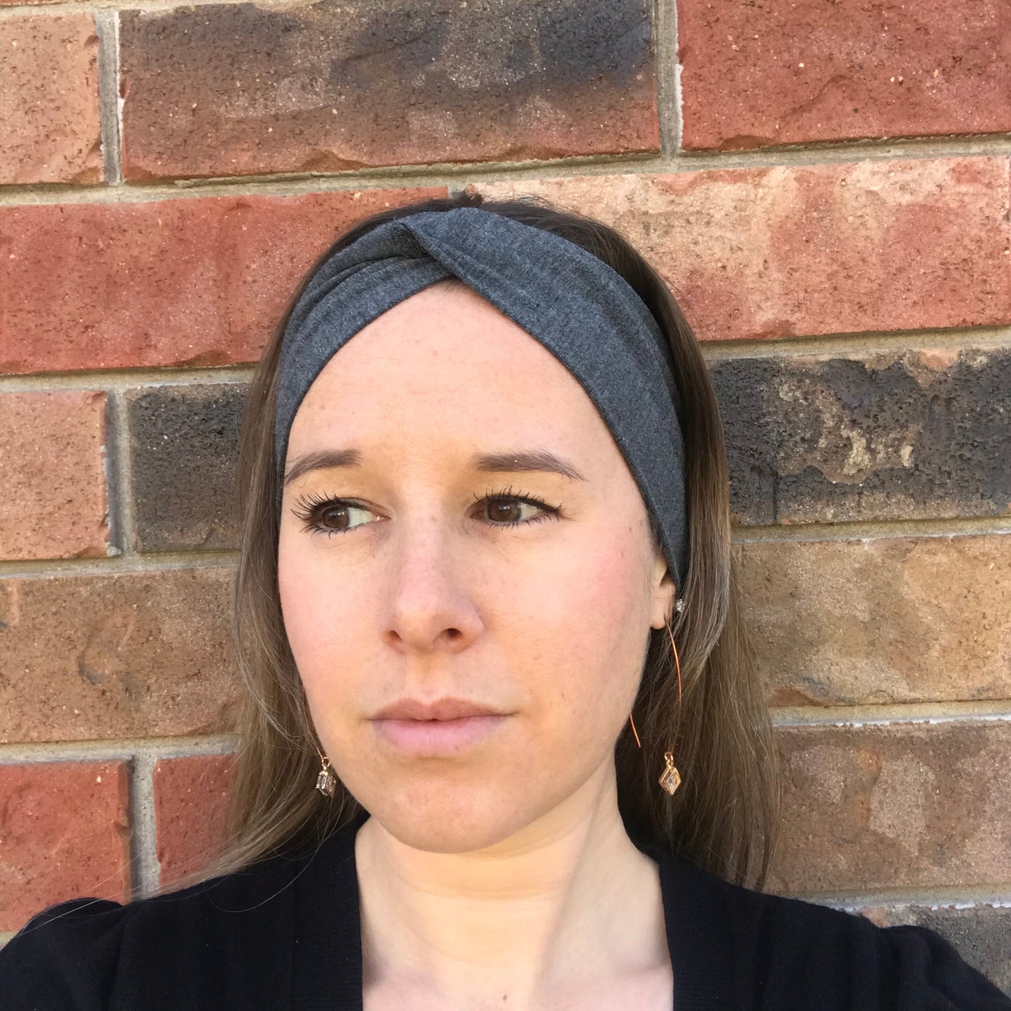 Dark gray twist headband with knotted center, worn across the forehead.