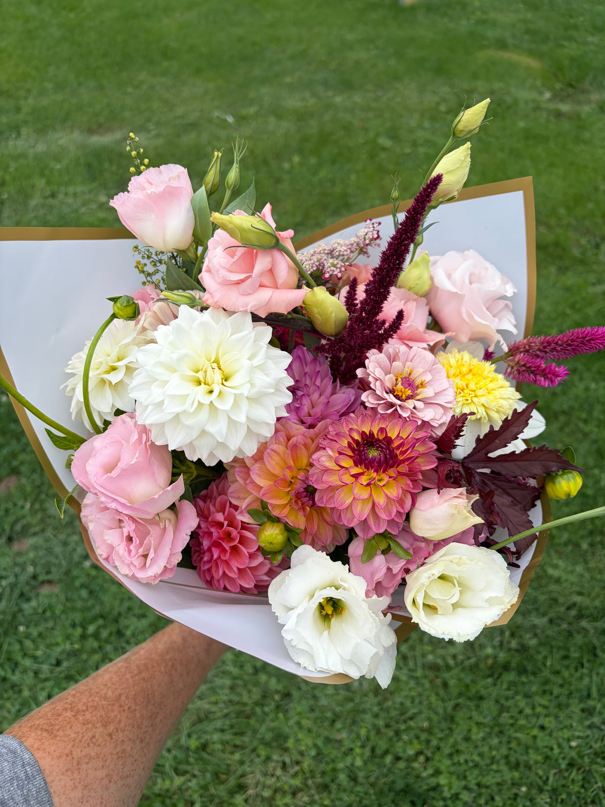 Fresh flower bouquet with pink roses, white flowers, and purple sprigs in paper wrap
