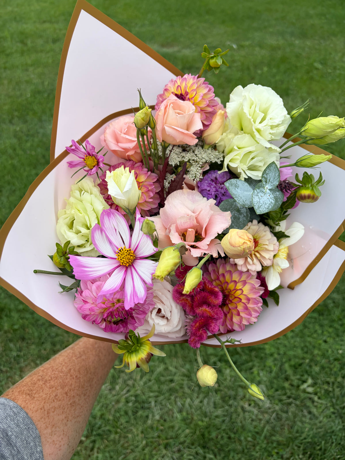 Fresh flower bouquet with pink roses, purple daisies, and pale green blooms in paper wrap