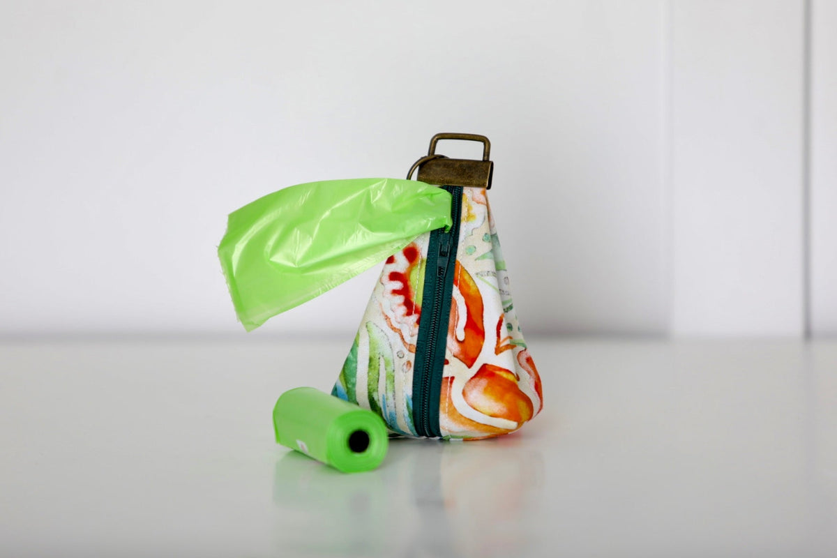 Keychain poop bag holder pouch with white base and colorful print, green bag and green roll.