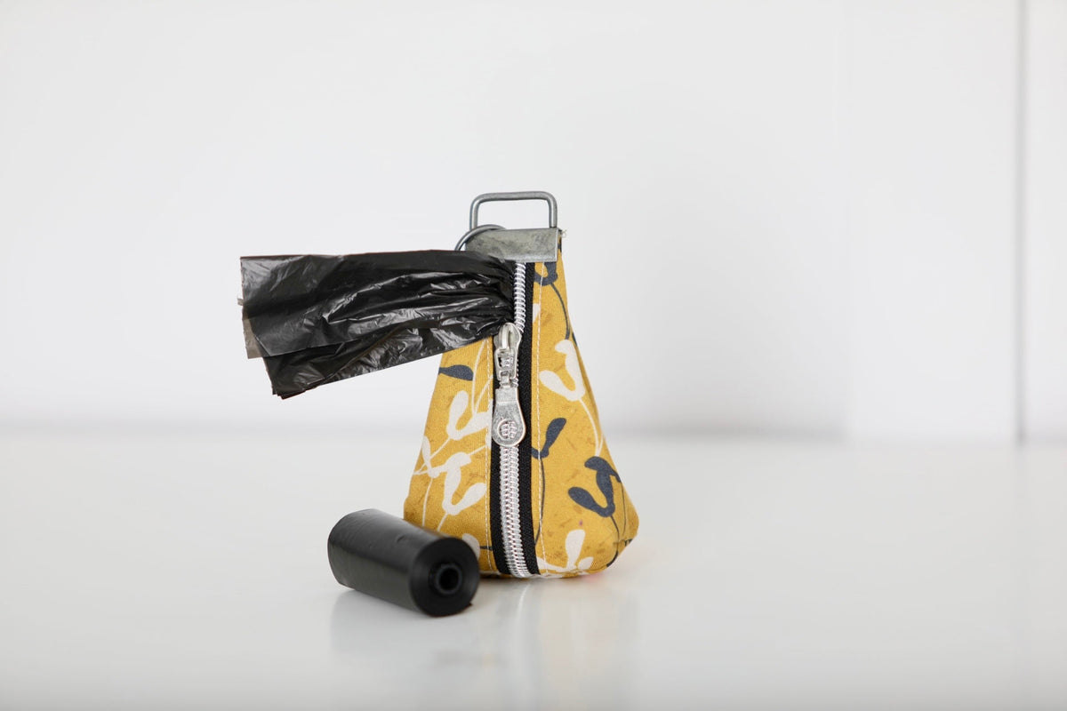 Keychain poop bag holder pouch with yellow abstract print and black back, black roll and bag.