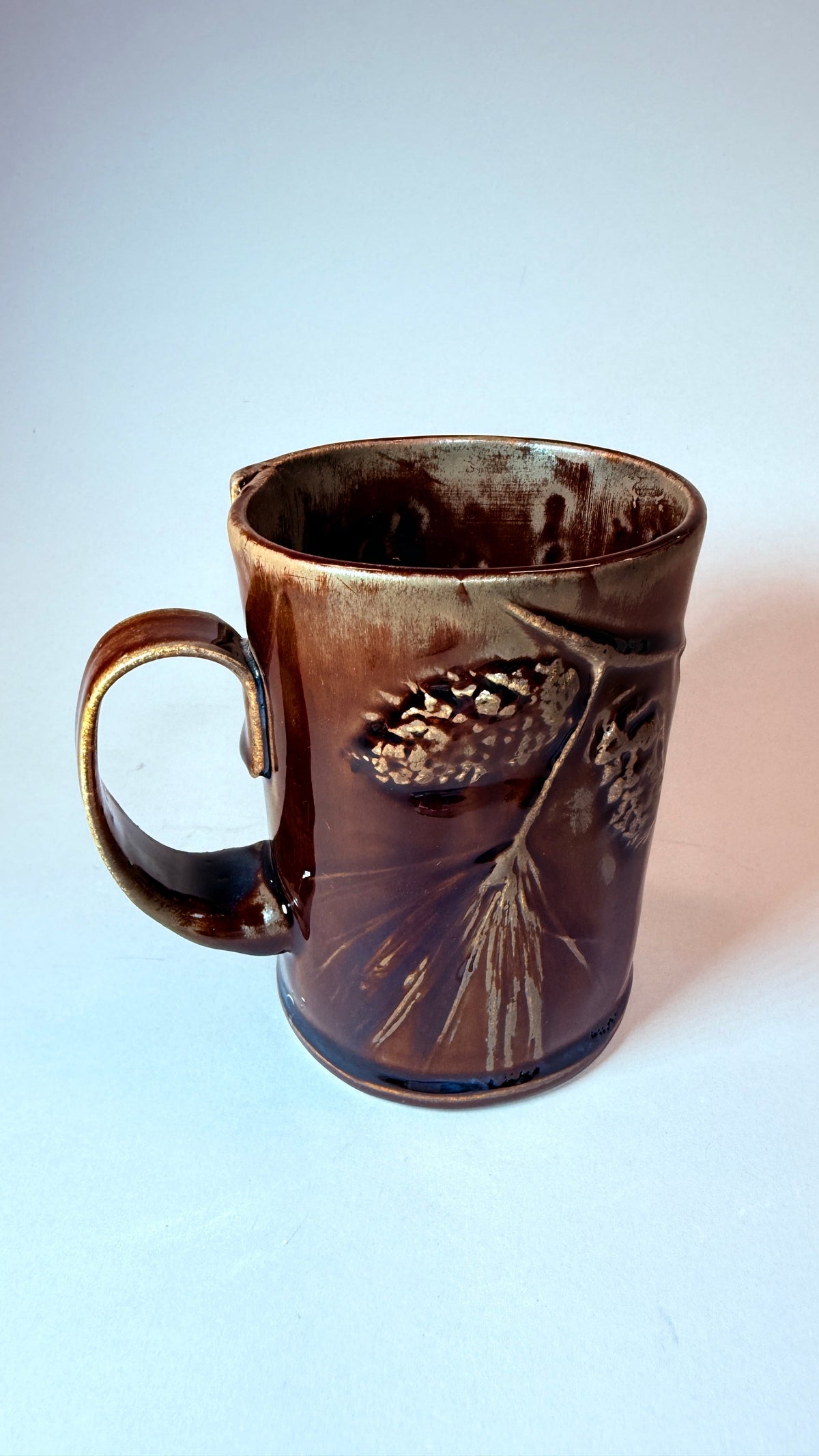 Brown ceramic mug with raised leaf design and side handle