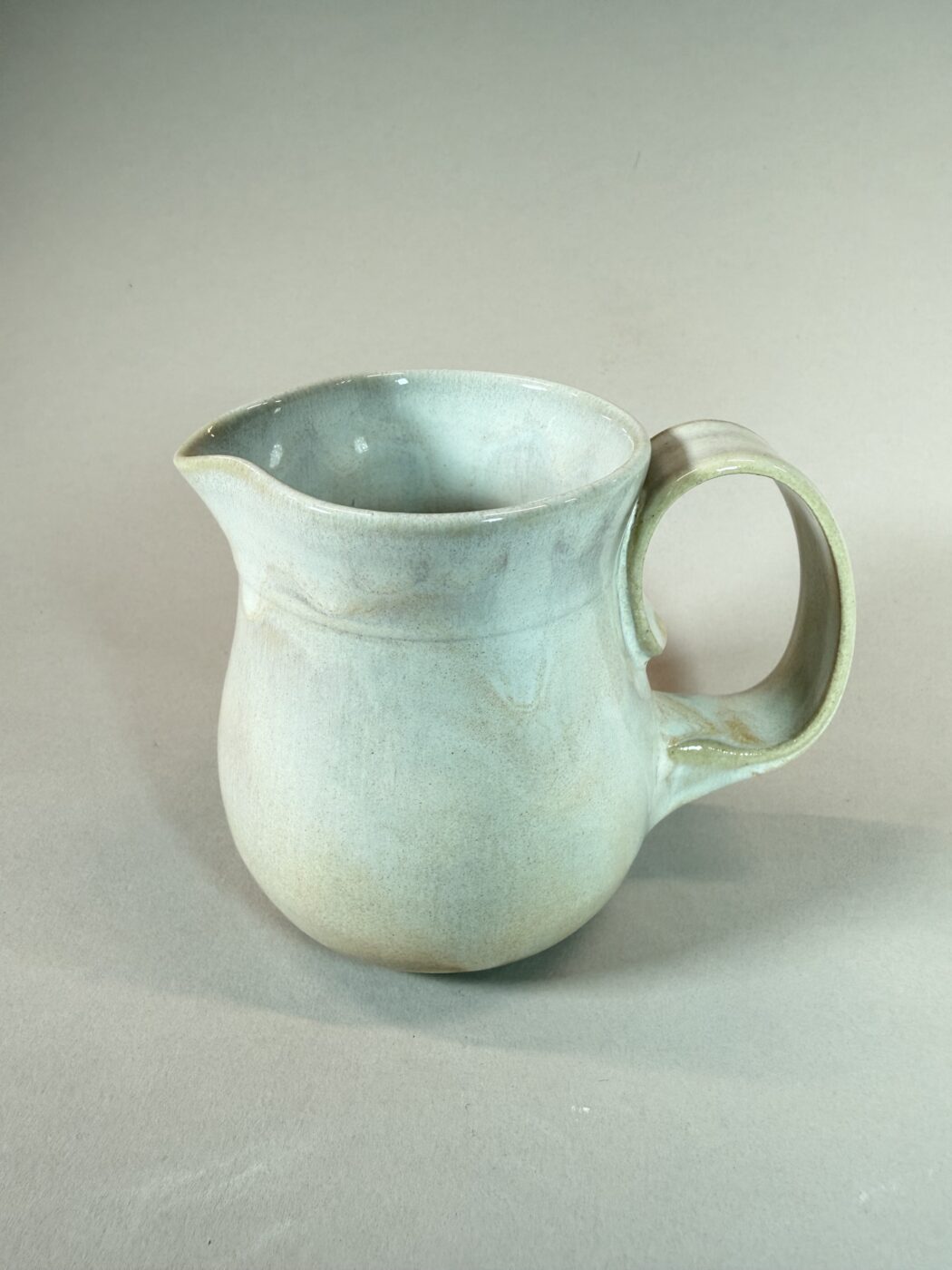 Light blue ceramic pitcher with curved spout and rounded handle, wide opening.