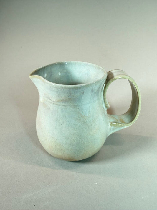 Light blue ceramic pitcher with curved spout and rounded handle, wide opening.
