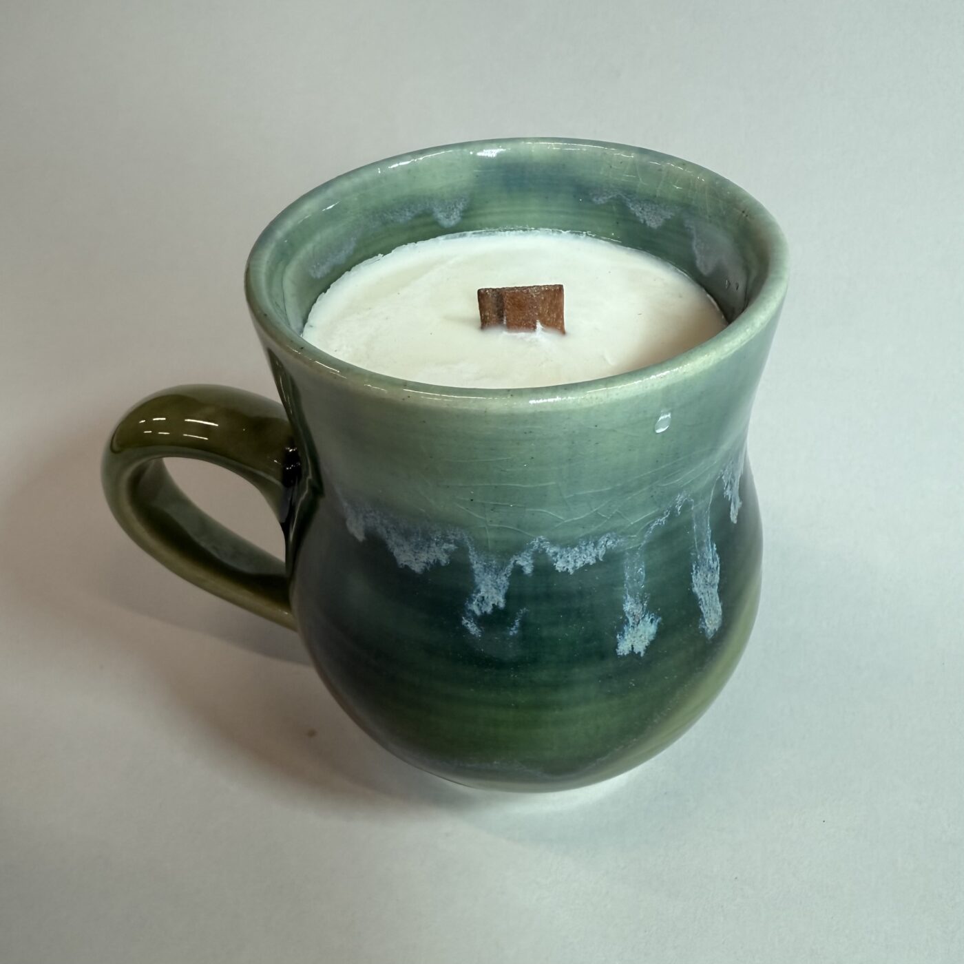 Green ceramic candle mug with side handle, filled with white wax and small center wick.