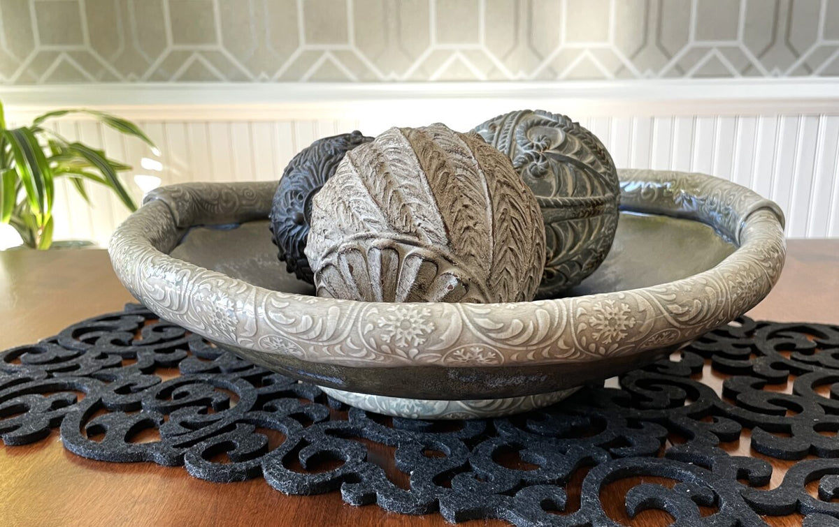 Ornate decorative bowl with textured silver rim and dark mottled interior, holding linens