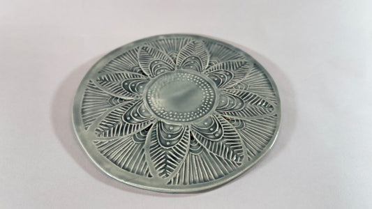 Round metal trivet with stamped floral mandala pattern, antiqued silver-gray finish