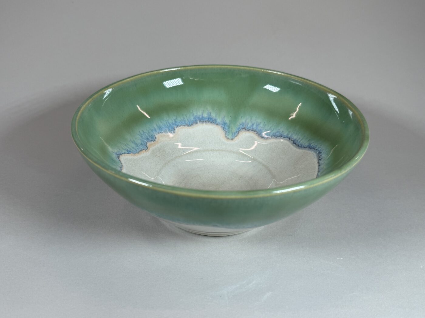 Green ceramic serving bowl with blue wave pattern inside, shallow round shape