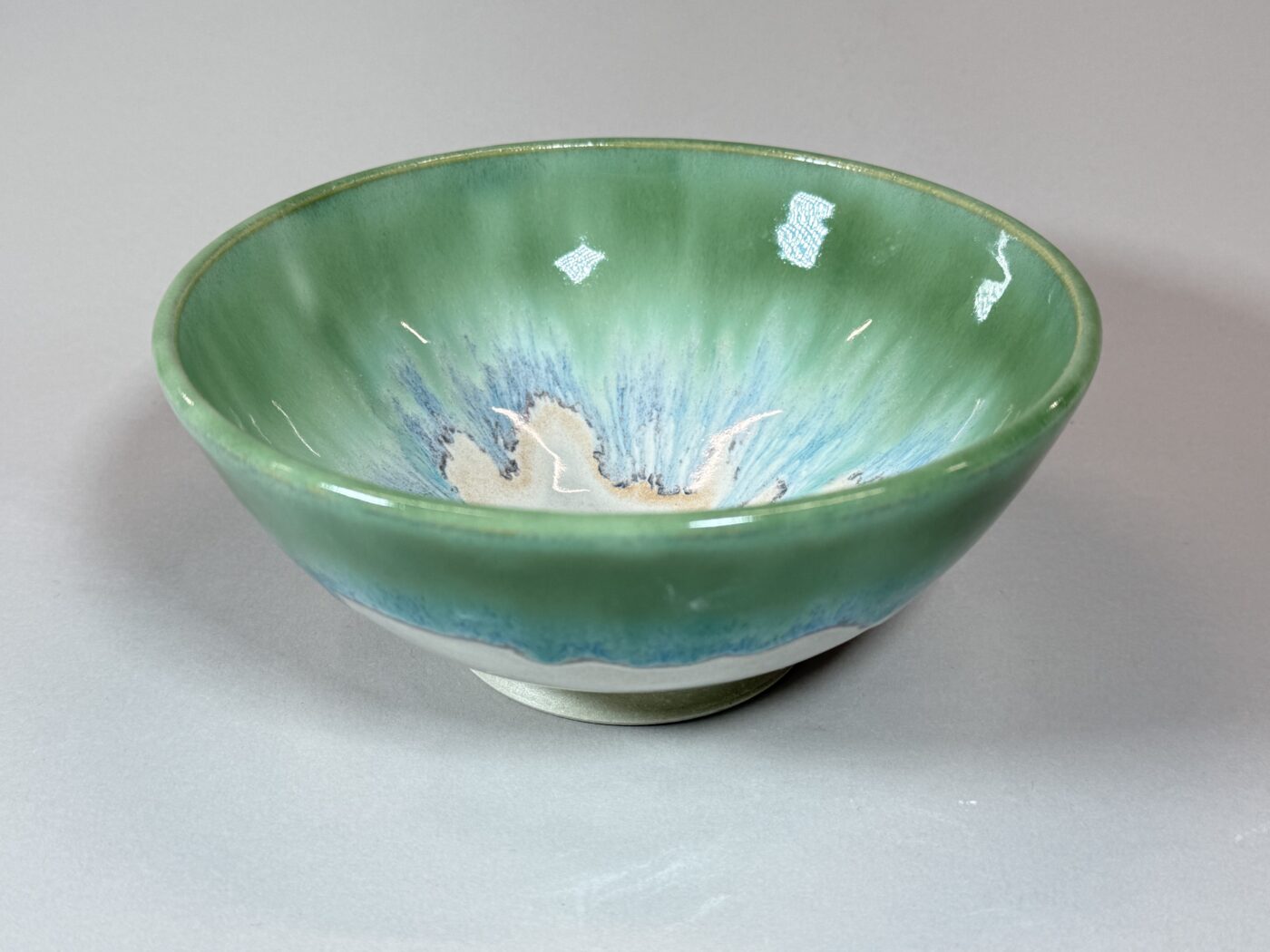 Glazed ceramic serving bowl with green rim and blue interior