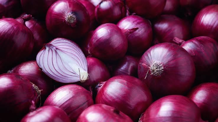 Pile of red onions, with one onion cut to show white purple layers