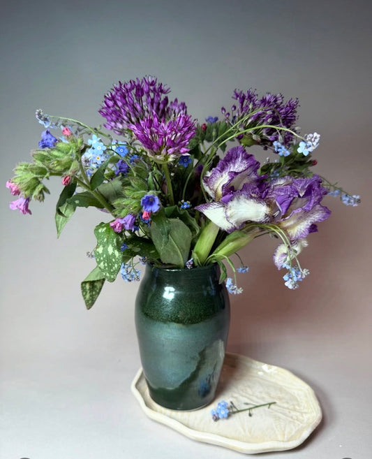 Green ceramic vase with glossy finish, holding a purple wildflower bouquet